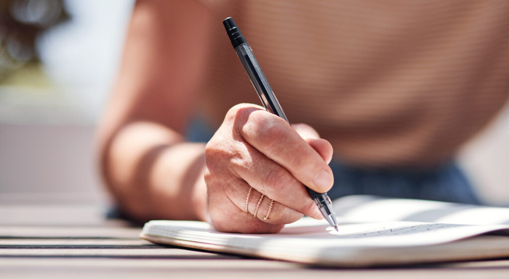 Cropped shot of an unrecognizable senior woman writing in her book outside on the balcony at home